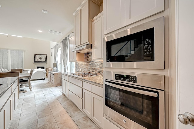 kitchen with decorative backsplash, stainless steel appliances, white cabinets, and light stone countertops