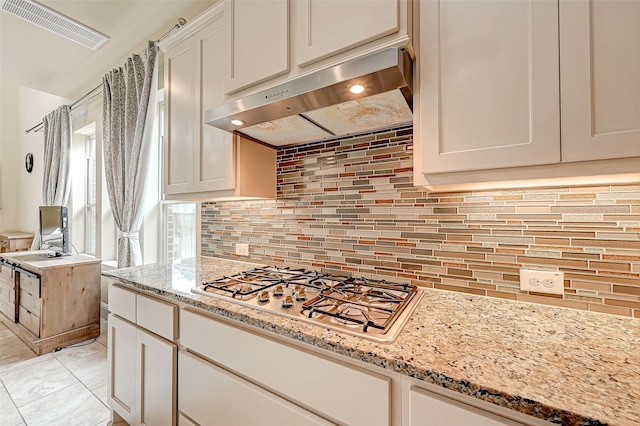 kitchen with stainless steel gas stovetop, decorative backsplash, light stone countertops, and white cabinetry