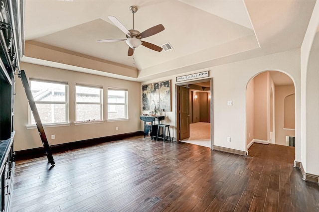 empty room with dark hardwood / wood-style flooring, a tray ceiling, and ceiling fan