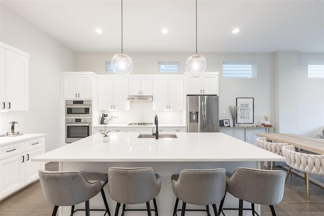 kitchen featuring appliances with stainless steel finishes, sink, decorative light fixtures, white cabinets, and an island with sink