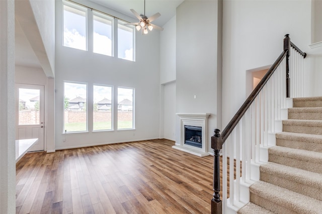 unfurnished living room with ceiling fan, a high ceiling, and hardwood / wood-style flooring