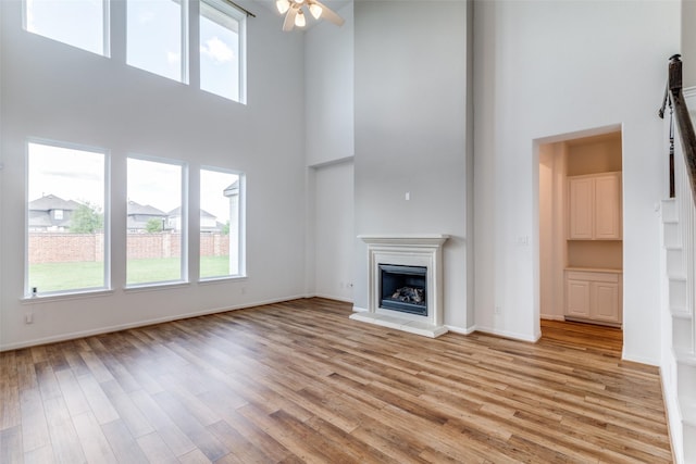 unfurnished living room with ceiling fan, a towering ceiling, and light hardwood / wood-style flooring