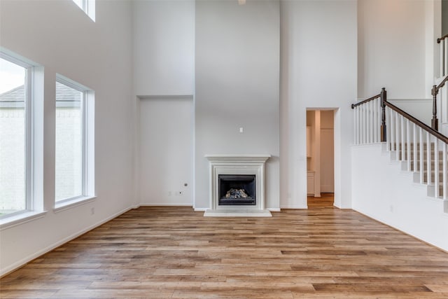 unfurnished living room featuring a wealth of natural light, light hardwood / wood-style flooring, and a high ceiling