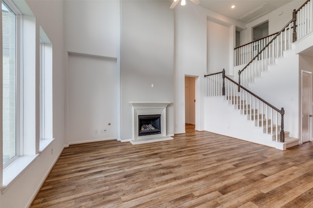 unfurnished living room with ceiling fan, a towering ceiling, and wood-type flooring