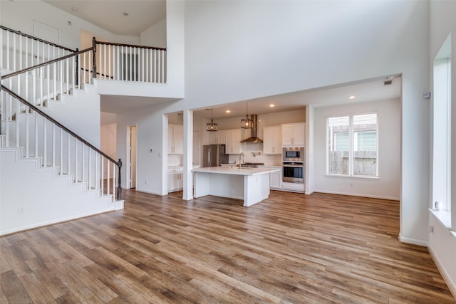 unfurnished living room with sink, a high ceiling, and light hardwood / wood-style flooring