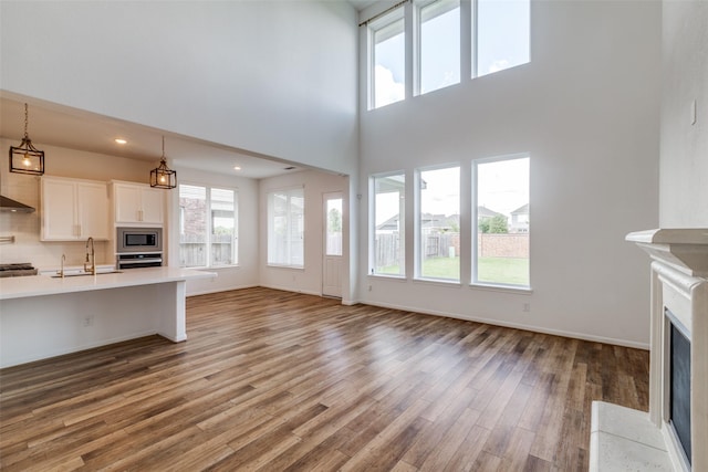 unfurnished living room with a wealth of natural light, hardwood / wood-style floors, a high ceiling, and sink