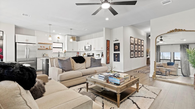 living room featuring ceiling fan, light hardwood / wood-style flooring, and sink