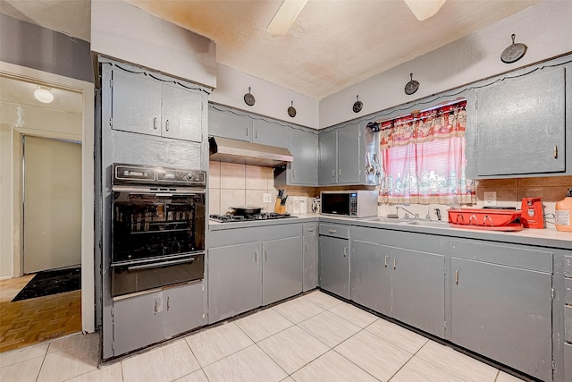 kitchen featuring backsplash, black oven, gray cabinets, and stainless steel gas cooktop