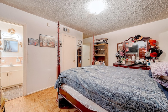 bedroom with light parquet floors, a textured ceiling, and ensuite bath