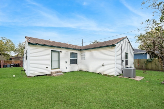 rear view of property with central air condition unit and a yard