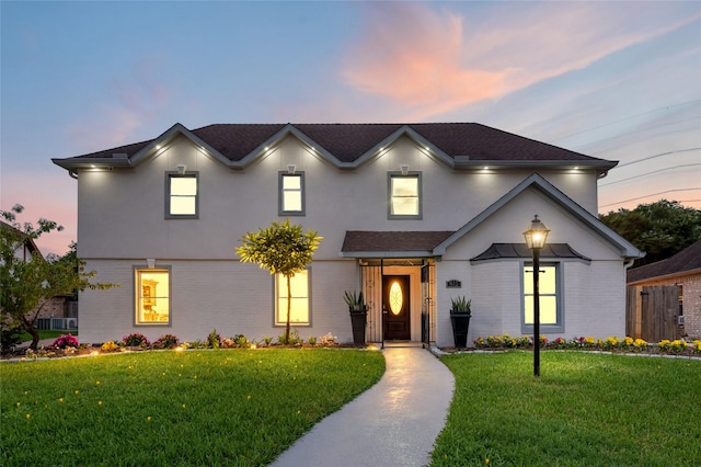 view of front of home featuring brick siding, a lawn, and stucco siding