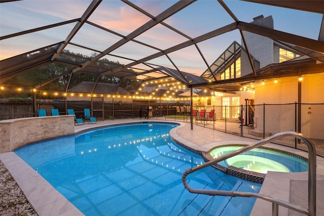 pool at dusk with glass enclosure, a patio, and a pool with connected hot tub