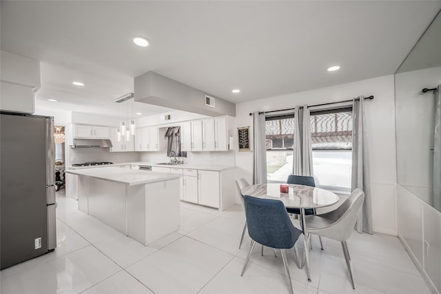 kitchen featuring light countertops, hanging light fixtures, freestanding refrigerator, white cabinetry, and a kitchen island