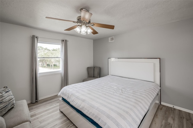 bedroom with ceiling fan, light hardwood / wood-style floors, and a textured ceiling