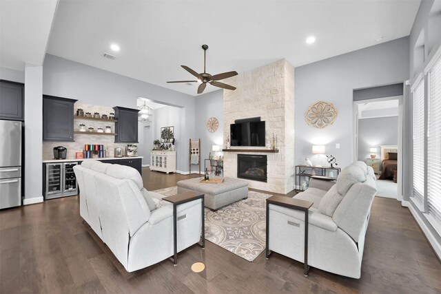 living room with beverage cooler, dark wood-type flooring, a fireplace, ceiling fan, and bar area