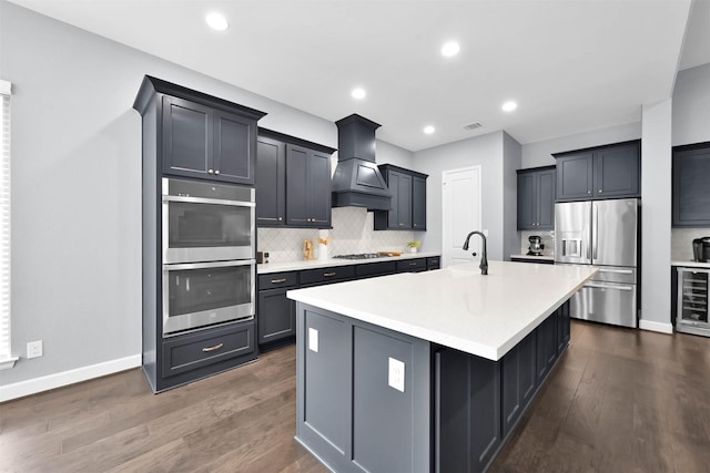 kitchen featuring a center island with sink, stainless steel appliances, dark hardwood / wood-style flooring, wine cooler, and custom range hood