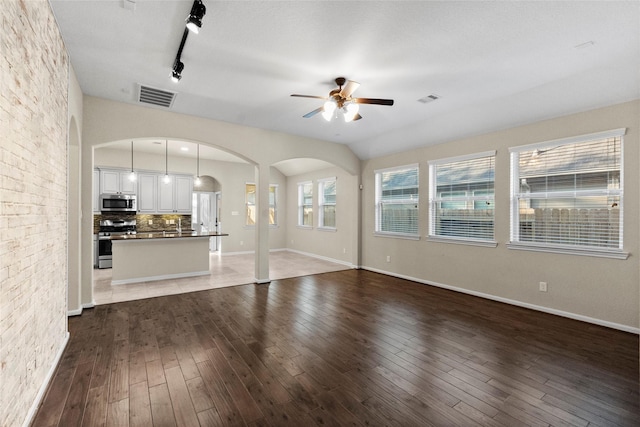 unfurnished living room featuring ceiling fan, rail lighting, and dark wood-type flooring