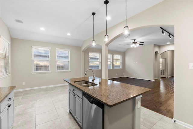 kitchen featuring sink, light hardwood / wood-style flooring, stainless steel dishwasher, dark stone counters, and a center island with sink