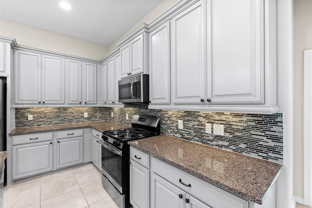 kitchen featuring gray cabinetry, dark stone counters, decorative backsplash, light tile patterned flooring, and appliances with stainless steel finishes