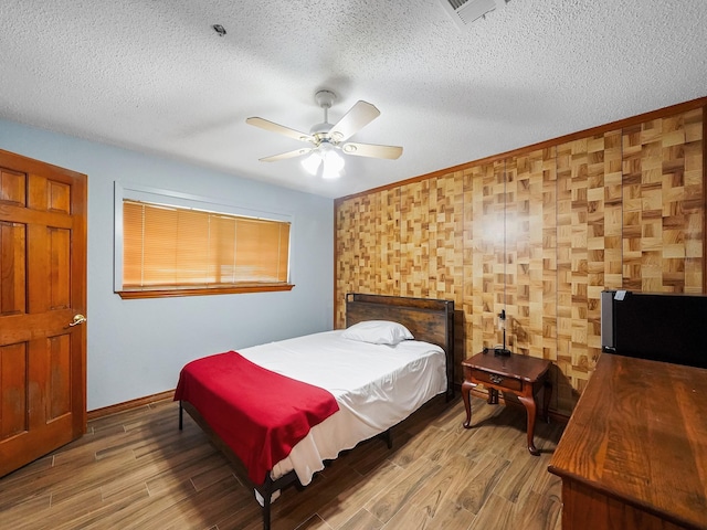 bedroom with ceiling fan, wood-type flooring, and a textured ceiling