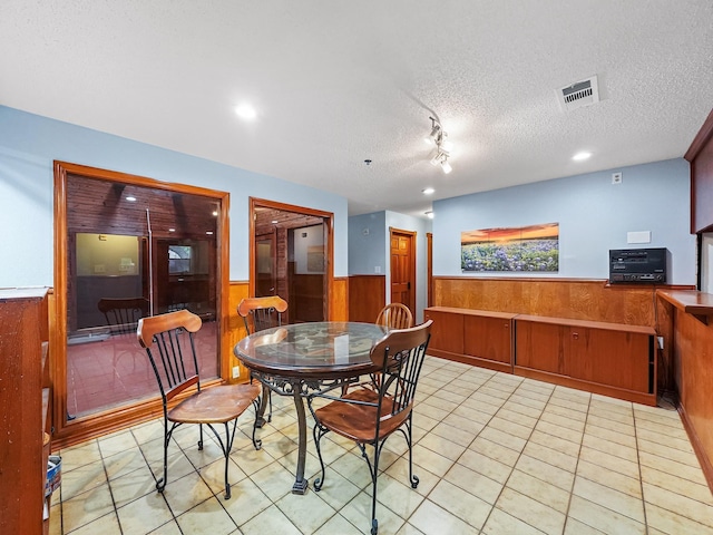 dining area featuring light tile patterned floors, a textured ceiling, and wooden walls