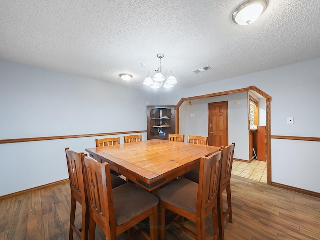 dining area with a textured ceiling, light hardwood / wood-style floors, and a notable chandelier