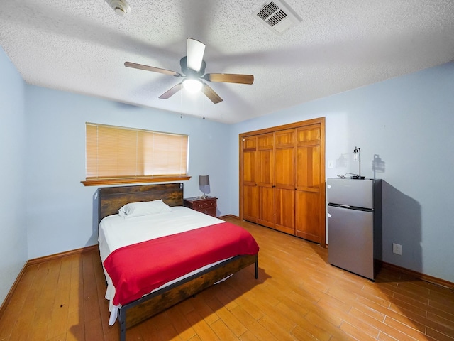 bedroom with light hardwood / wood-style flooring, ceiling fan, a textured ceiling, stainless steel refrigerator, and a closet