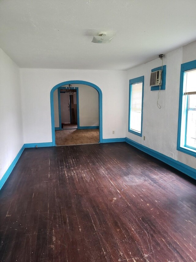 unfurnished room featuring dark hardwood / wood-style floors, an AC wall unit, and a chandelier