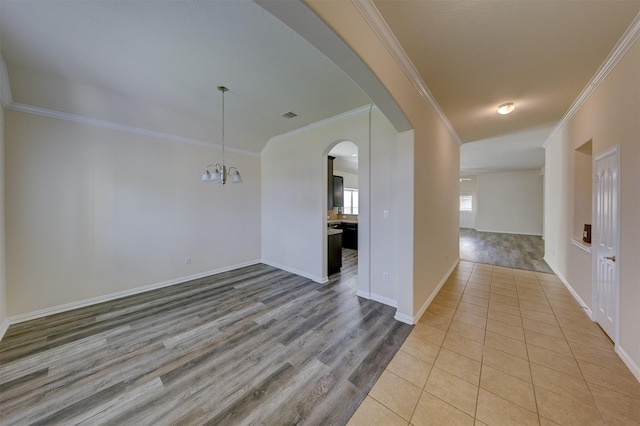 spare room with crown molding, a chandelier, and light wood-type flooring