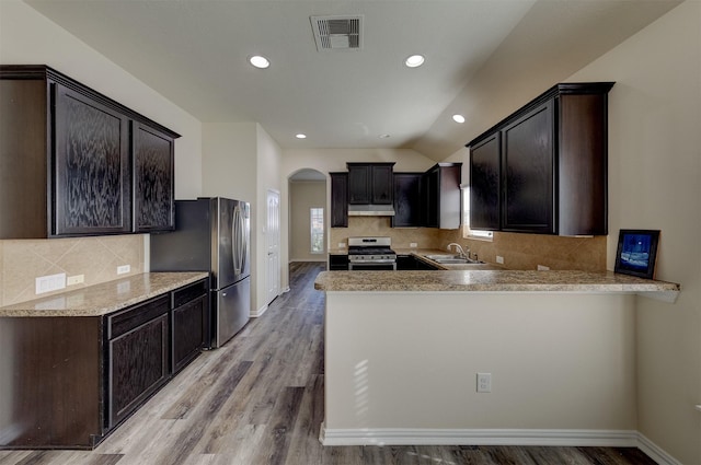 kitchen with kitchen peninsula, appliances with stainless steel finishes, dark brown cabinetry, sink, and light hardwood / wood-style floors