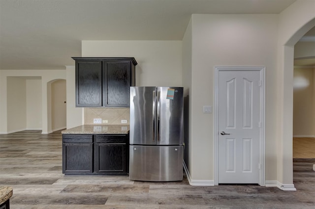 kitchen featuring decorative backsplash, light wood-type flooring, stainless steel refrigerator, and light stone countertops