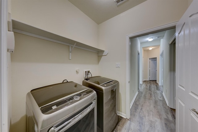 washroom featuring a textured ceiling, washing machine and dryer, and light hardwood / wood-style floors