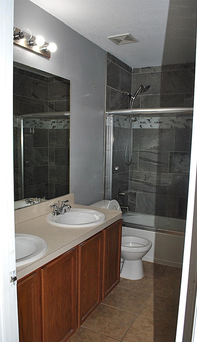 full bathroom with vanity, combined bath / shower with glass door, tile patterned flooring, toilet, and a textured ceiling