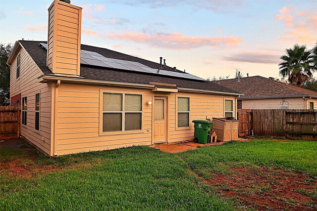 back house at dusk featuring solar panels and a yard