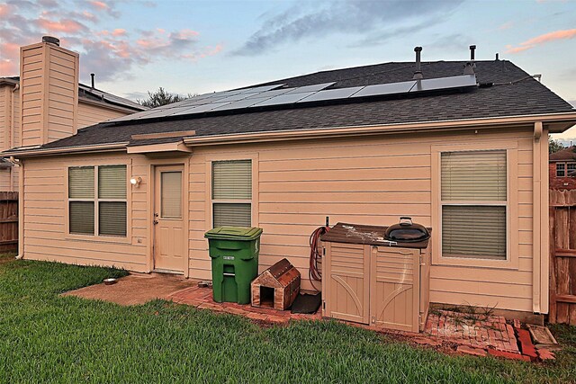 back house at dusk featuring a lawn and solar panels