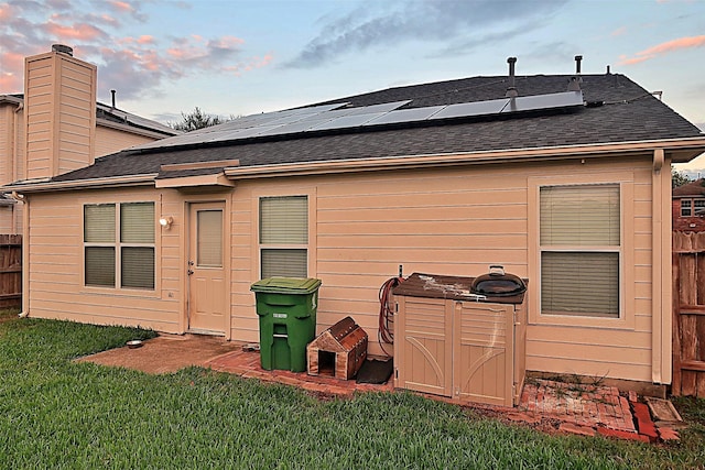 rear view of property featuring solar panels, fence, a lawn, and roof with shingles