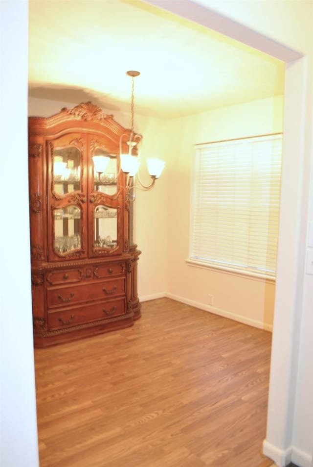 unfurnished dining area featuring light wood-style floors, baseboards, and an inviting chandelier