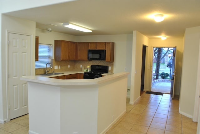 kitchen with light tile patterned floors, a sink, decorative backsplash, black appliances, and brown cabinetry