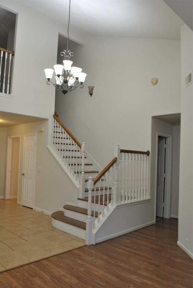 stairway with a notable chandelier, wood finished floors, a towering ceiling, and baseboards