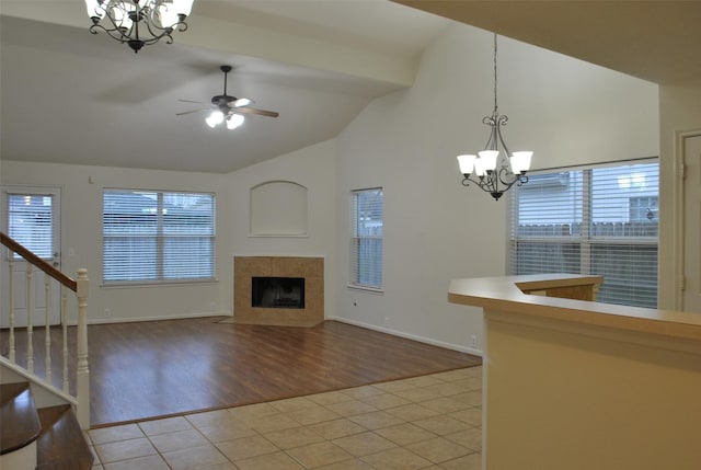 unfurnished living room featuring light tile patterned floors, baseboards, a tile fireplace, stairway, and ceiling fan with notable chandelier