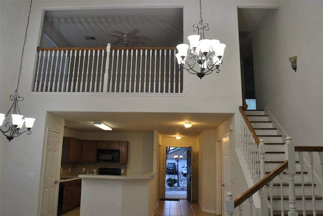 stairway featuring ceiling fan with notable chandelier, tile patterned flooring, and a towering ceiling