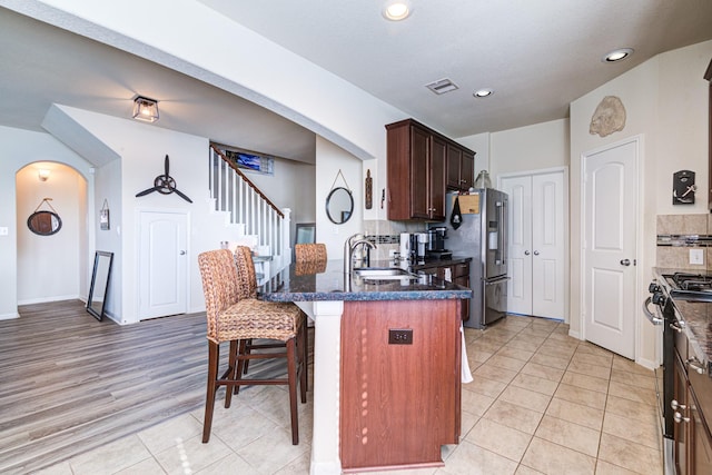 kitchen with sink, a kitchen breakfast bar, decorative backsplash, appliances with stainless steel finishes, and light wood-type flooring