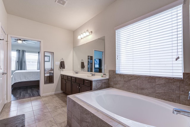 bathroom with tiled bath, ceiling fan, vanity, and a healthy amount of sunlight