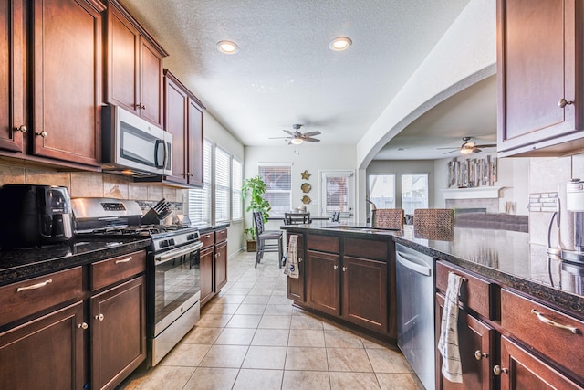 kitchen featuring decorative backsplash, appliances with stainless steel finishes, a tile fireplace, and dark stone countertops