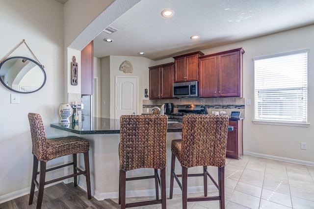 kitchen with a kitchen bar, appliances with stainless steel finishes, backsplash, and kitchen peninsula