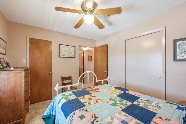 bedroom with ceiling fan, a closet, light colored carpet, and a textured ceiling