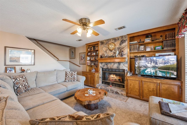 carpeted living room with a stone fireplace, ceiling fan, and a textured ceiling