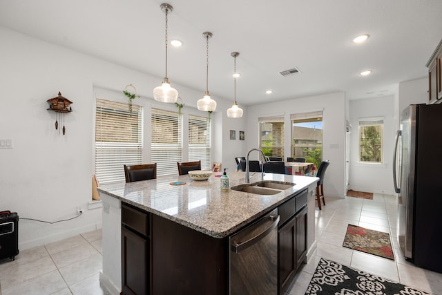 kitchen with dark brown cabinetry, sink, light stone counters, an island with sink, and appliances with stainless steel finishes