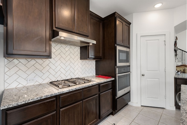 kitchen with light stone countertops, appliances with stainless steel finishes, tasteful backsplash, dark brown cabinets, and light tile patterned floors