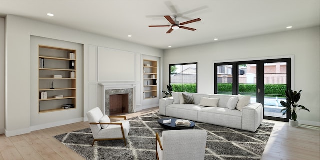 living room with ceiling fan, french doors, built in features, a fireplace, and light wood-type flooring